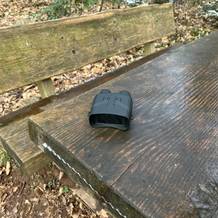 Das Relassy NV4000 Nachtsichtgerät liegt auf einer feuchten Holztischplatte im Wald. Im Hintergrund sind eine Holzbank und herbstliches Laub zu sehen.