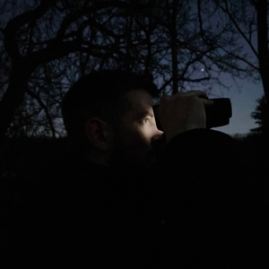 Ein Mann nutzt das Nachtsichtgerät Relassy NV4000 bei Dunkelheit im Wald. Das Gerät leuchtet sein Gesicht leicht an, die Umgebung bleibt dunkel.