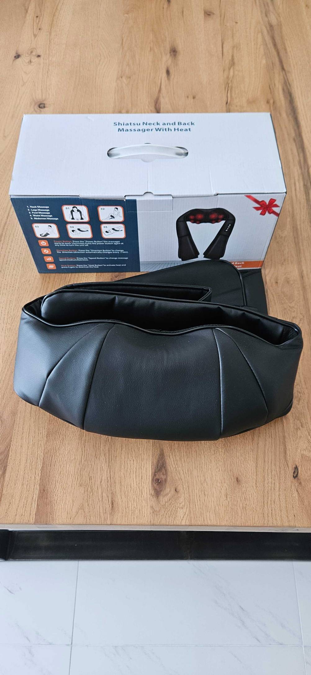 Vor der Originalverpackung liegt ein getestetes Nackenmassagegerät zusammengefaltet.