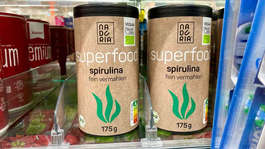 Mehrere Dosen Spirulina stehen nebeneinander in einem Verkaufsregal.