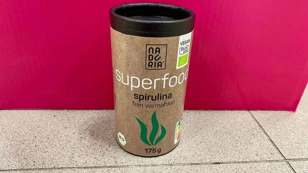 Eine Dose Spirulina im Test vor einer pinken Wand.