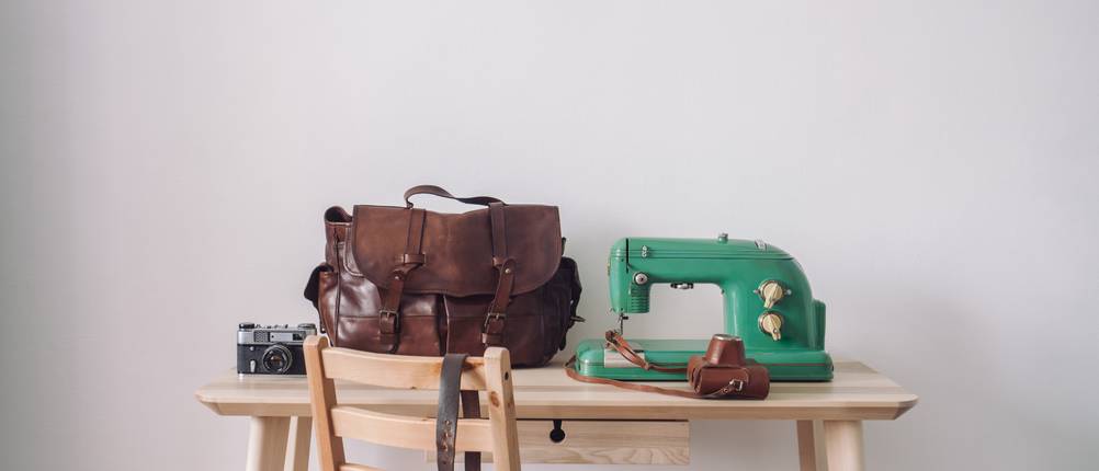 auf einem Holztisch steht eine Ledertasche und eine grüne Nähmaschine