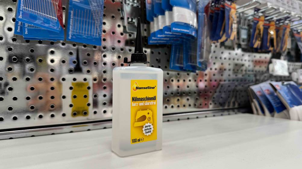 Ein getestetes Nähmaschinenöl steht auf einem Verkaufsregal im Hintergrund andere Produkte.