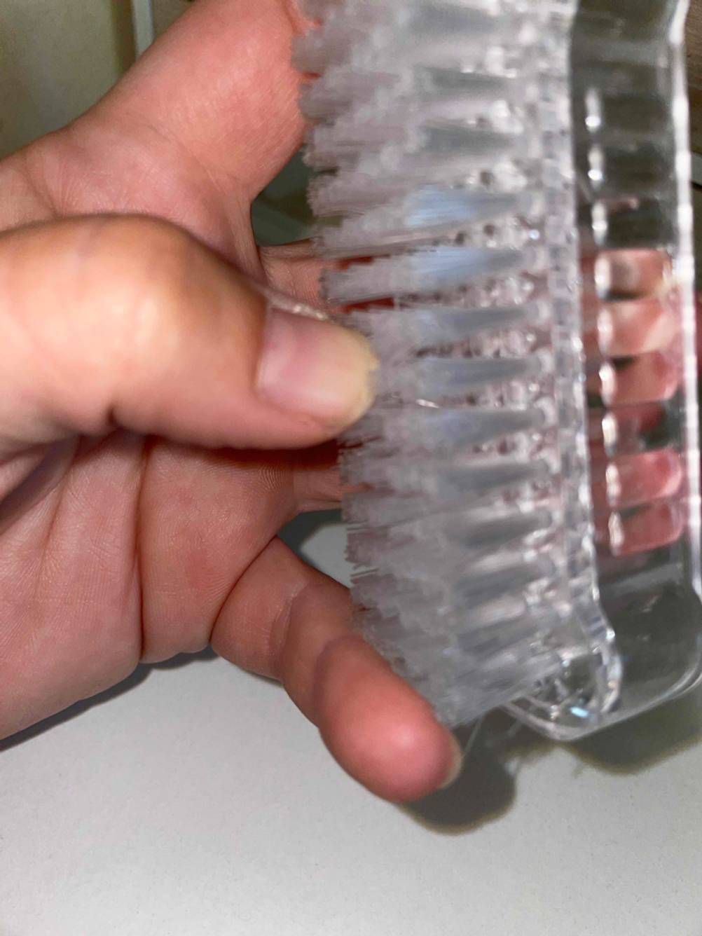 Eine Hand streift in Detailansicht über die Borsten einer getesteten Nagelbürste.