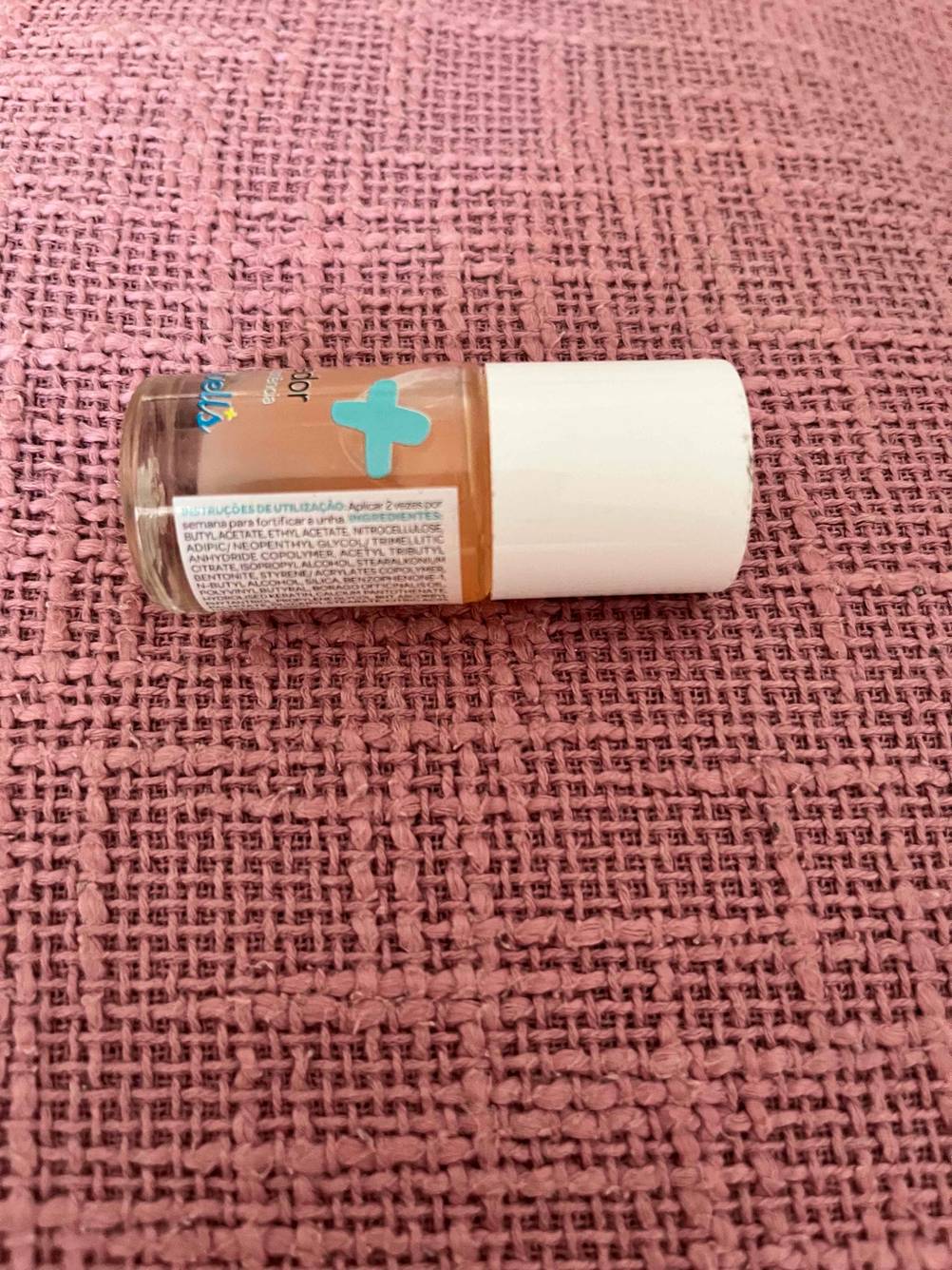 Eine Flasche des getesteten Nagelhärters horizontal auf einer pinken Oberfläche.