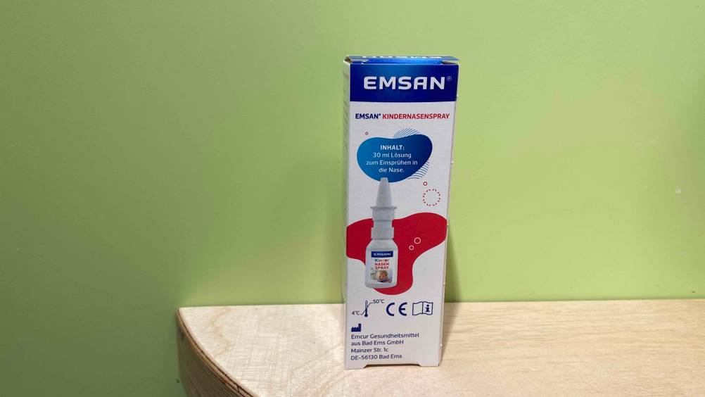Rückseite einer Packung des getesteten Kindernasensprays auf einem Holztisch vor einer grünen Wand.