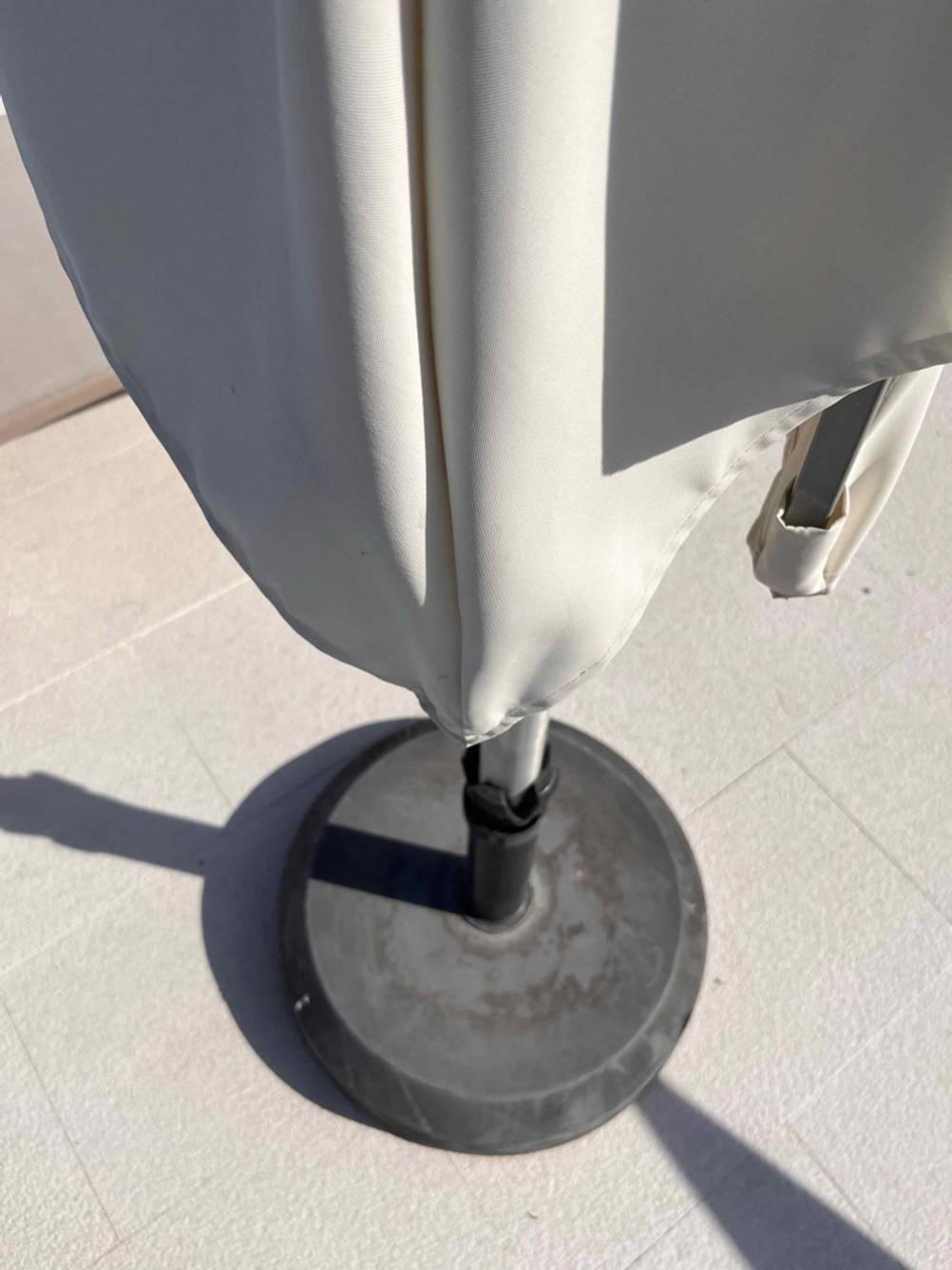 Sonnenschirme im Test: Detailansicht des weißen Stoffs sowie einem grauen Sonnenschirm-Ständer auf weißen Fliesen.