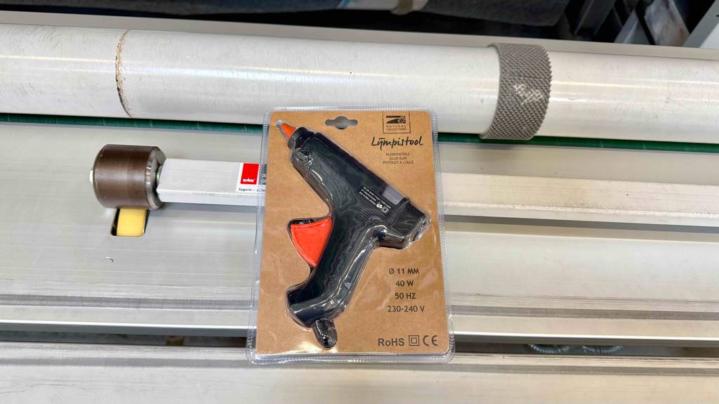 Die getestete 11-mm-Heißklebepistole liegt innerhalb der Verpackung auf einem weißen Regal.
