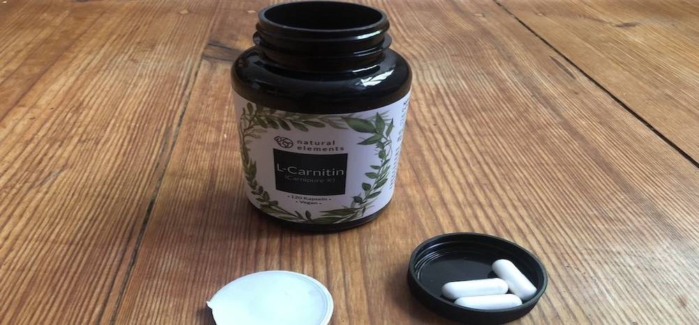 fatburner-test: Auf einem Tisch steht eine Kapseldose von Natural Elements. Neben der Dose liegt der Deckel mit drei Kapseln.