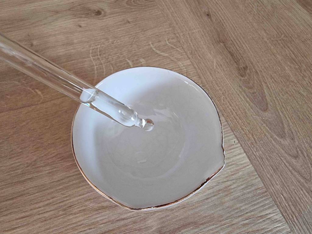 Vitamin-D-Präparat-Test: Glaspipette mit Flüssigkeit über einem weißen Behälter auf einer Holzfläche.