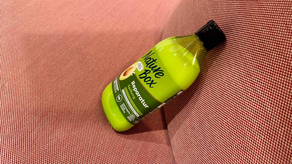 Seitenansicht der Flasche der getesteten Nature-Box-Spülung auf einem roten Polster.