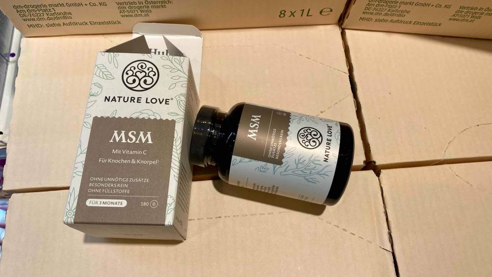 Im Test: Eine Dose MSM-Kapseln liegt neben der Verpackung auf Kartonagen.