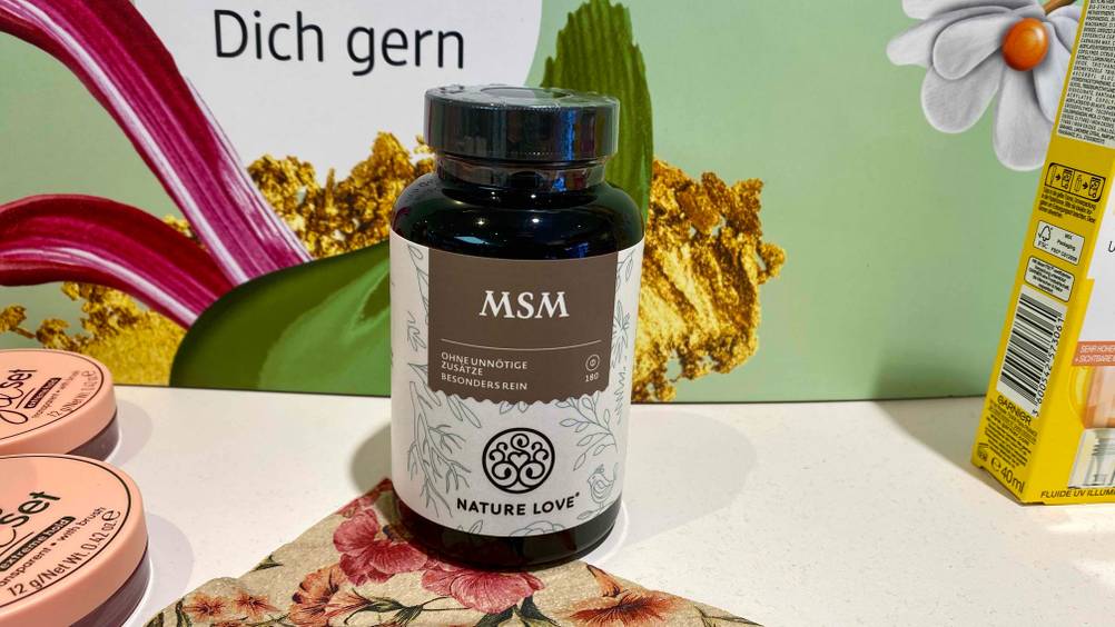 Getestet: Eine Dose MSM-Kapseln steht zwischen anderen Produkten vor einem Plakat.