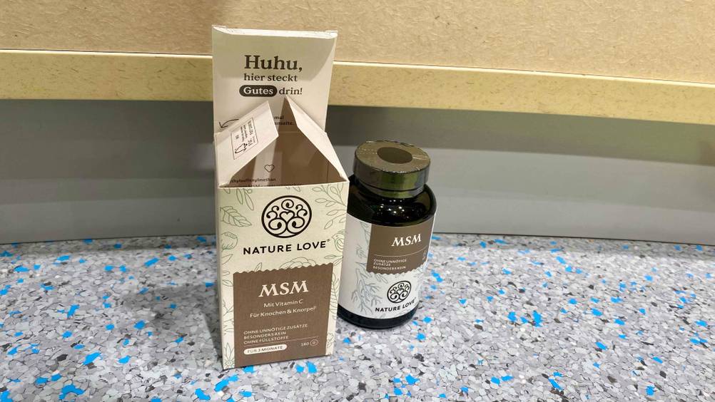 MSM-Kapseln getestet: Eine Dose steht neben der Originalverpackung auf einem blau-grauen Boden.