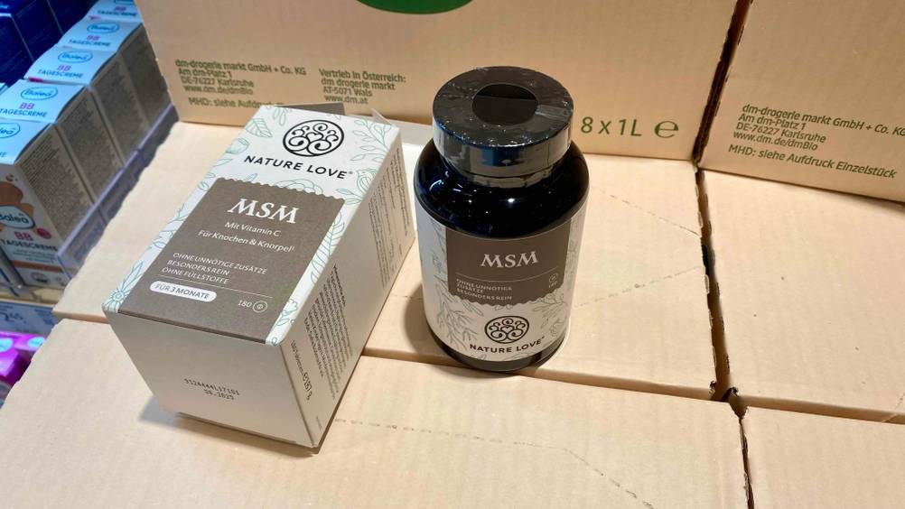 Eine Dose getestete MSM-Kapseln steht neben der liegenden Originalverpackung auf Kartons.