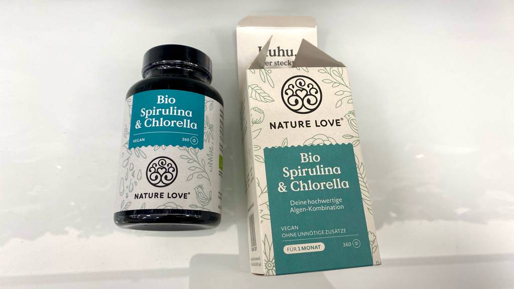 Eine geöffnete Verpackung und getestete Spirulina-Chlorella-Tabletten im lichtdichten Fläschchen liegen auf einer weißen Oberfläche.