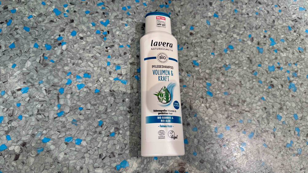 Auf einem blau-grauen Boden liegt eine Flasche des Naturkosmetik-Shampoo im Test.