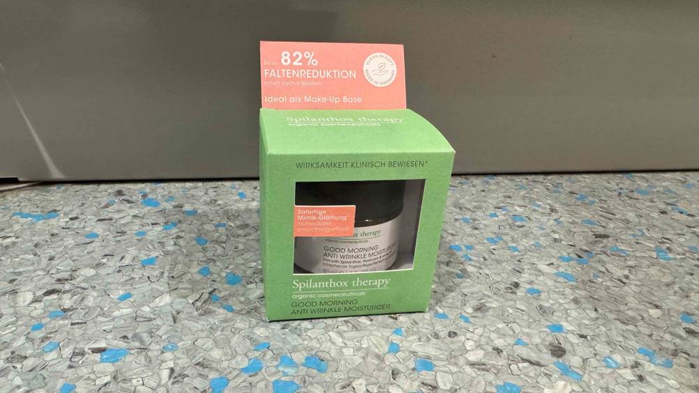 Vor einer grauen Wand am Boden steht die verpackte Naturkosmetik-Tagescreme im Test.