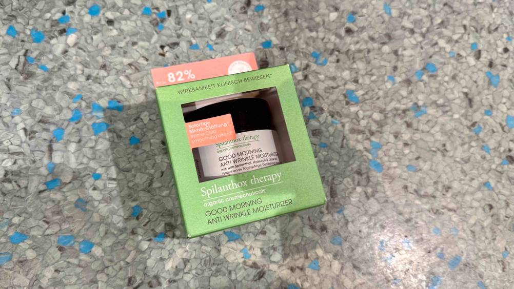 Eine verpackte Naturkosmetik-Tagescreme im Test auf einem grau-blauen Boden liegend.