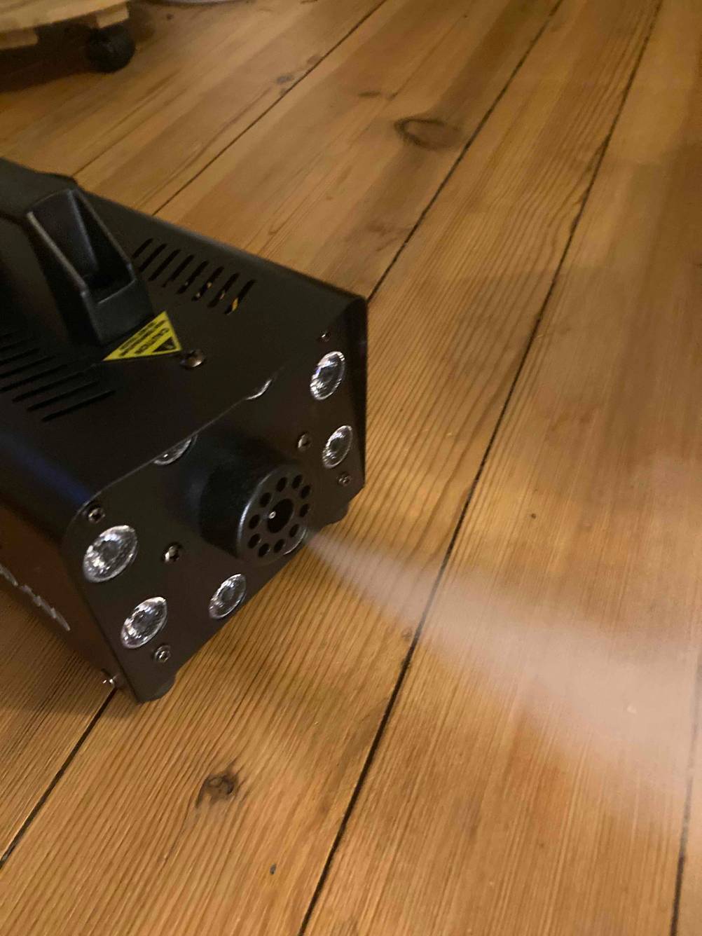 Eine Nebelmaschine im Test die Nebel versprüht auf einem Holzboden.