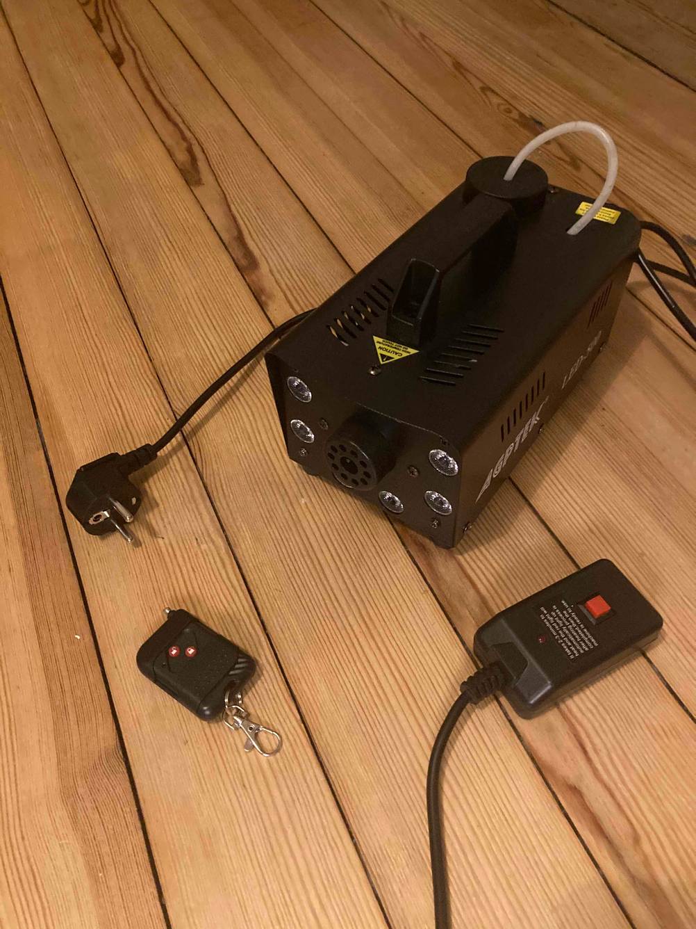 Eine getestete Nebelmaschine mit Zubehör auf einem Holzboden.
