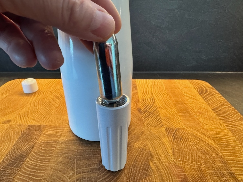 Eine Hand legt eine Kapsel in den Aufsatz des Nemt-Sahnespenders