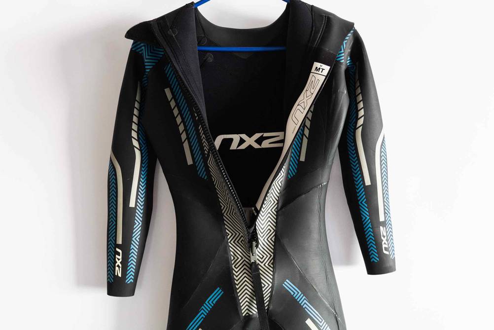 Ein getesteter Triathlon-Neoprenanzug mit geöffnetem Reisverschluss an einem Bügel vor einer hellen Wand hängend.