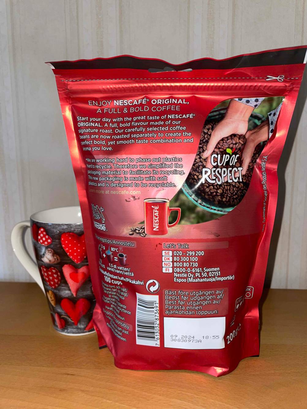 Ein roter wiederverschließbarer Nescafé Standbeutel mit löslichem Kaffee im Test steht neben einer Tasse auf einem Holzuntergrund.