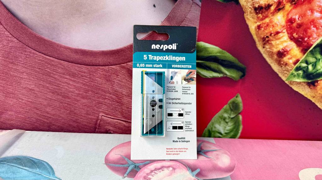 Im Test: Die Trapezklingen befinden sich innerhalb ihrer Verpackung vor einem roten Plakat mit Pizzamotiv.