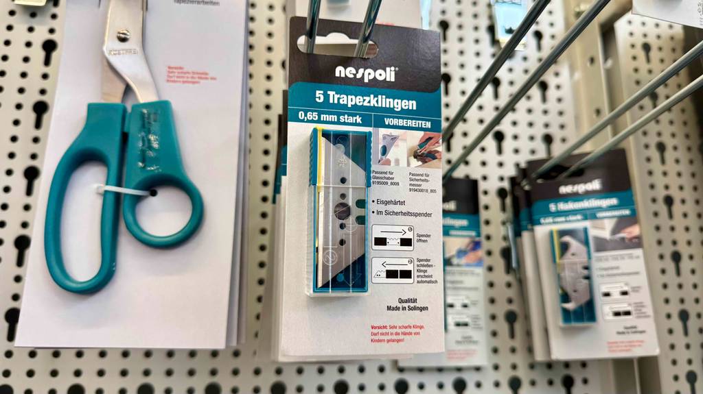 Die getesteten Trapezklingen hängen innerhalb ihrer 5er-Packung an einem Regal neben Scheren und Hakenklingen.