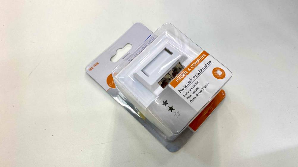Eine getestete Netzwerkdose in der transparenten Originalverpackung auf einer hellen Fläche.