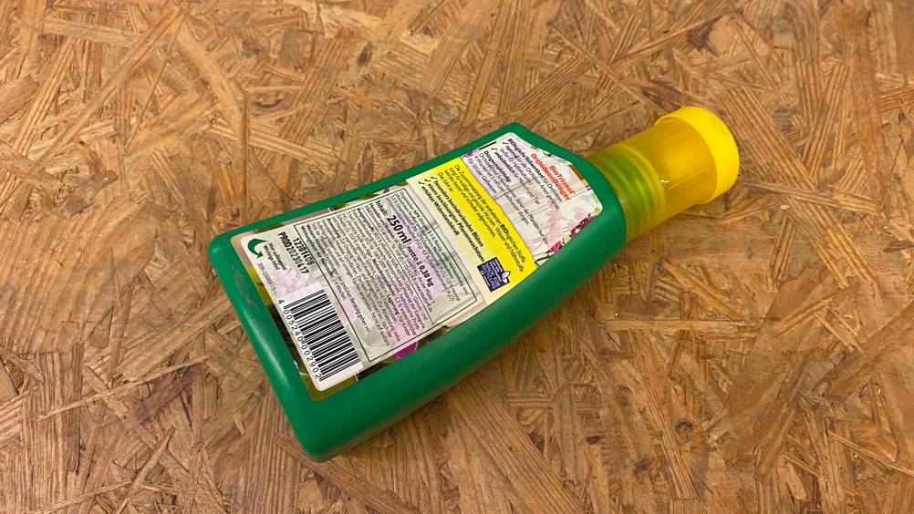 Eine grüne Flasche mit getestetem Orchideendünger liegt mit Sicht auf den rückseitigen Beschreibungs-Aufkleber auf einem Holzuntergrund.
