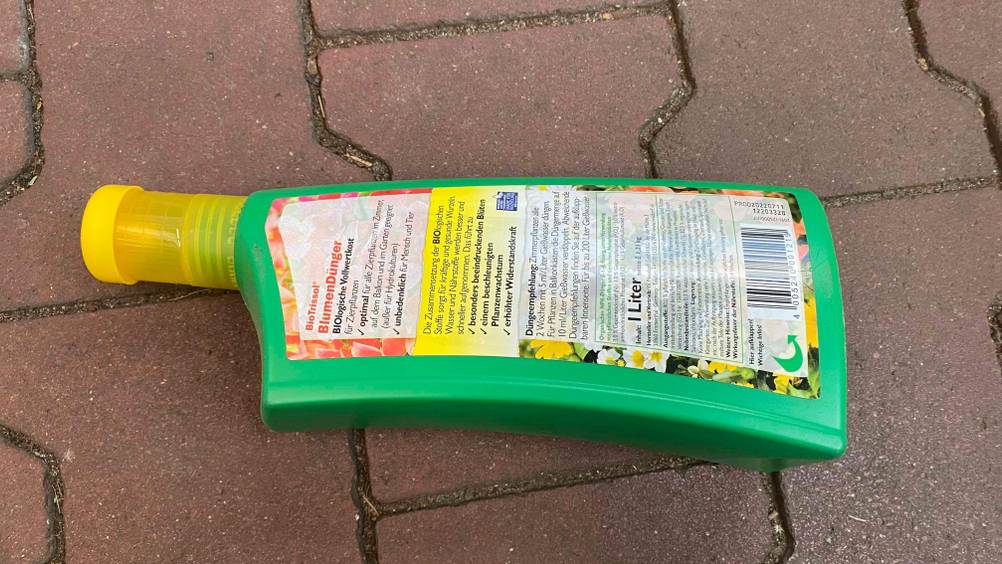 Grüne 1-Liter-Kunststoffflasche mit Blumendünger im Test, mit Blick auf die rückwärtige Produktbeschreibung.