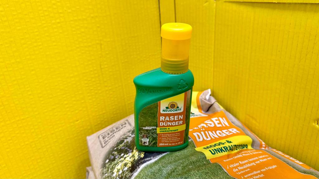 Eine Flasche flüssiger Rasendünger steht zum testen auf einem Sack.
