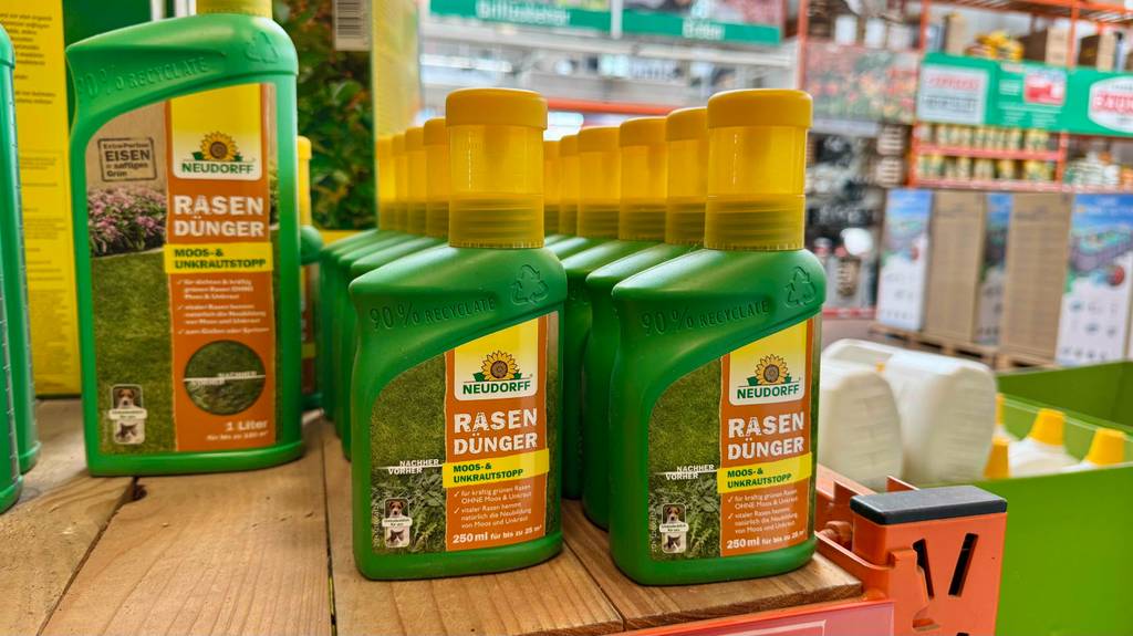 Im Test: Mehrere Flaschen flüssiger Rasendünger stehen neben- und hintereinander zwischen anderen Produkten.