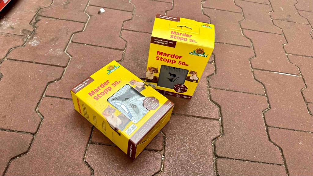 Zwei gelbe Originalverpackungen mit jeweils einem Marderschreck im Test befinden sich auf einem Terrakotta-Boden.