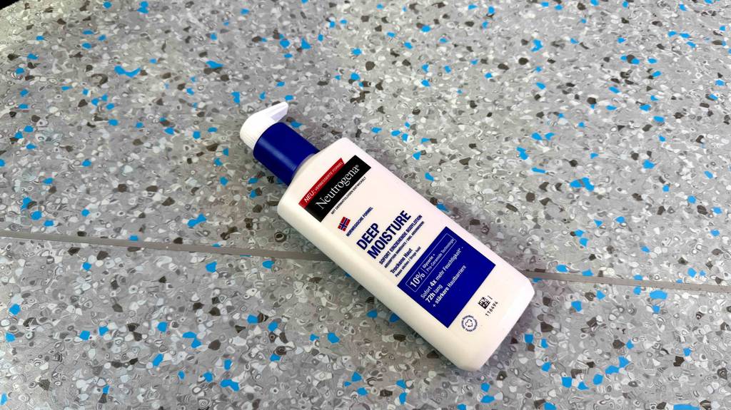 Eine Flasch getestete Körperlotion für sehr trockene Haut liegt auf einem gesprenkelten Boden.
