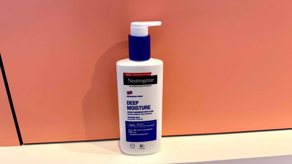Eine Flasche Körperlotion für sehr trockene Haut steht zum testen auf einem weißen Regal vor einer lachsfarbenen Wand.