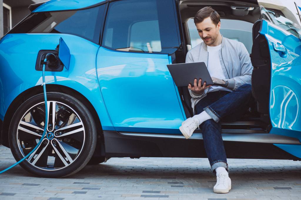 Ein Mann sitzt in einem Elektroauto und schaut auf seinen Laptop.