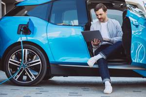 Neuwagen-Rabatt-Test: Ein Mann sitzt in einem Elektroauto und schaut auf seinen Laptop.