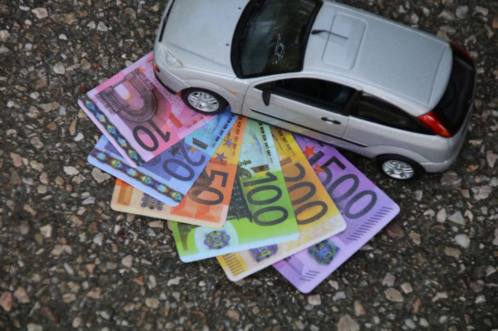 Ein Modellauto steht auf Euroscheinen, die auf einem Steinboden liegen.