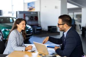 Ein junge Frau unterschreibt einen Vertrag nach erfolgreicher Verhandlung im Autohaus.