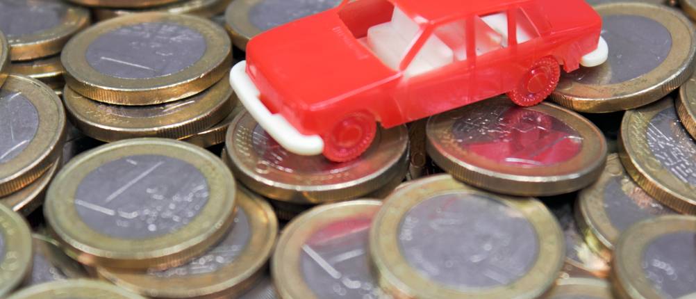 Neuwagen-Rabatt-Test: Ein rotes Spielzeug-Auto steht auf einem Haufen von 1-Euro-Münzen.