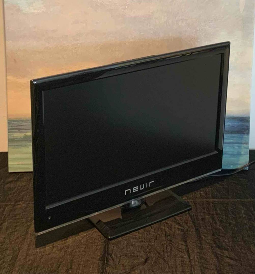 Im Test: Ein kleiner Fernseher steht auf einem dunklen Tisch vor einem Bild.