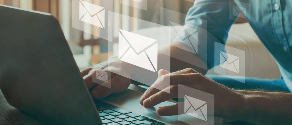 Newsletter-Software-Test: Ein Mann sitzt vor einem Laptop, aus dessen Display Briefumschläge fliegen.