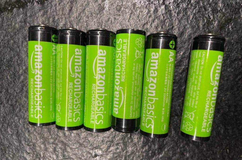 AA-Akkus im Test: Sechs grüne NiMH-Akkus der Marke AmazonBasics liegen nebeneinander auf einem schwarzen, unebenen Untergrund.