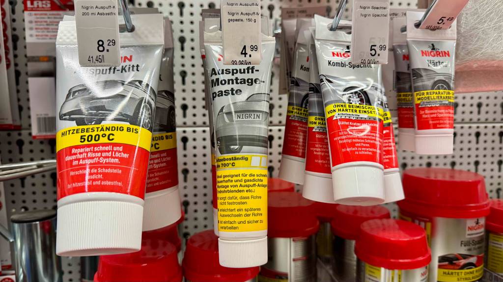 Auspuff-Montagepaste im Test: Mehrere Tuben hängen zwischen anderen Produkten in einem Regal.