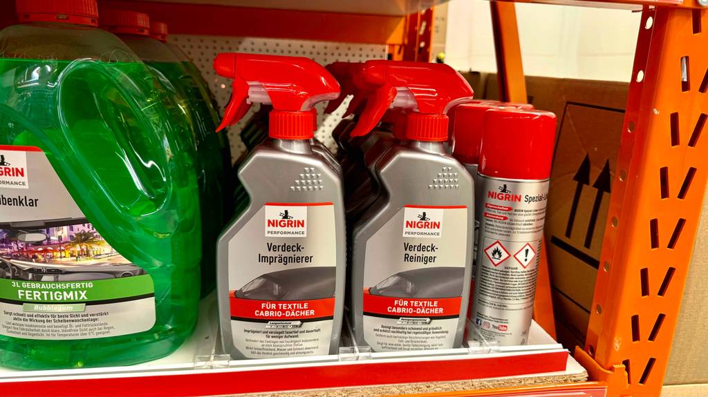 Im Test: Mehrere Sprühflaschen Cabrioverdeck-Imprägnierung stehen hintereinander zwischen anderen Produkten in einem Regal.