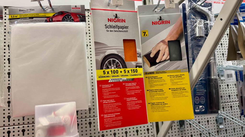 Schleifpapier im Test: Mehrere Packungen unterschiedlicher Ausführungen hängen in einem Regal zwischen anderen Produkten.