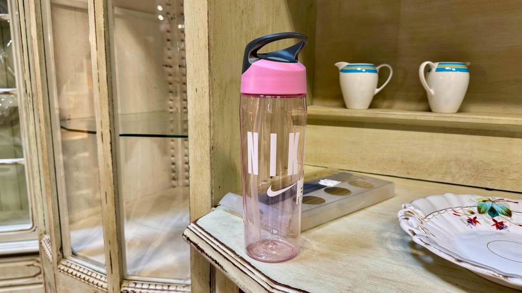 Eine Trinkflasche mit Strohhalm steht zum testen in einem Holzregal neben Porzellan.
